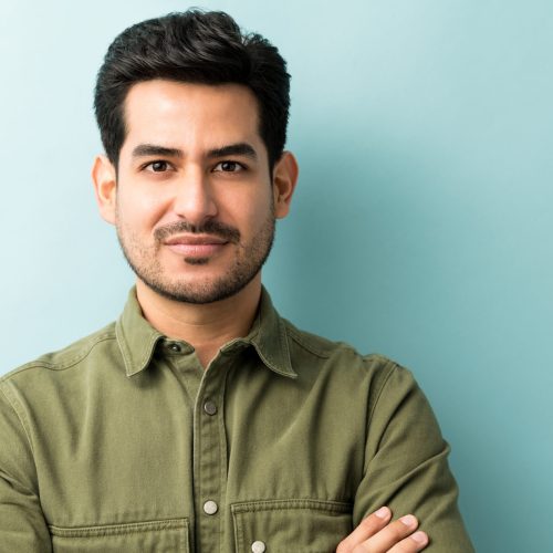 Man Standing Against Blue Background Closeup of young Hispanic man in casuals at studio